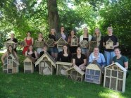 Junge Frauen stehen auf einer Wiese vor Insektenhotels