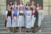 Zwölf junge Frauen im Dirndl stehen auf einer Treppe