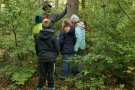 WEZ-Mitarbeiter steht vor Baum und erklärt Kindern woran man eine Baumart erkennt