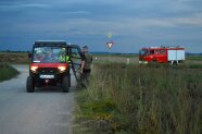 Ein Mann steht auf einem Feldweg, redet mit Rettungskräften der Feuerwehr in einem Quad 