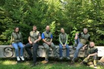 2 Frauen und 4 Männer in Forstkleidung sitzen auf Holzbalken im Wald 