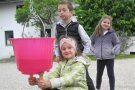 Drei Kinder üben Melken an einem Eimer mit künstlichem Euter