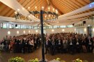 Viele Personen sitzen in einem voll besetzten Saal und klatschen