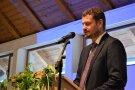 Mann steht am Mikrofon und hält eine Rede